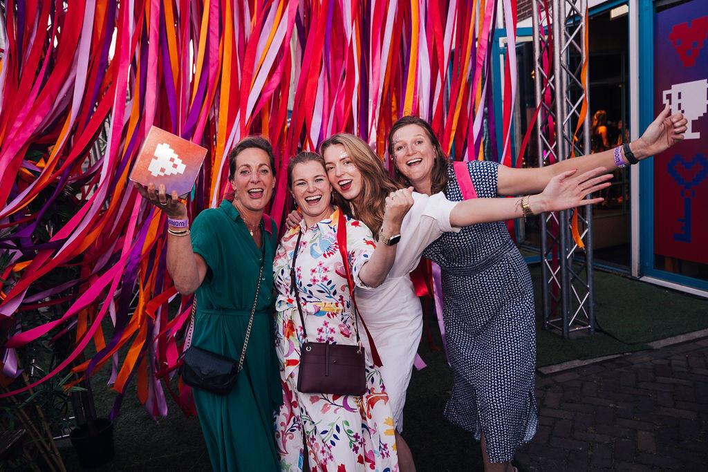 Vier vrouwen poseren met Best Workplaces 2024 award voor gekleurd lintjesgordijn