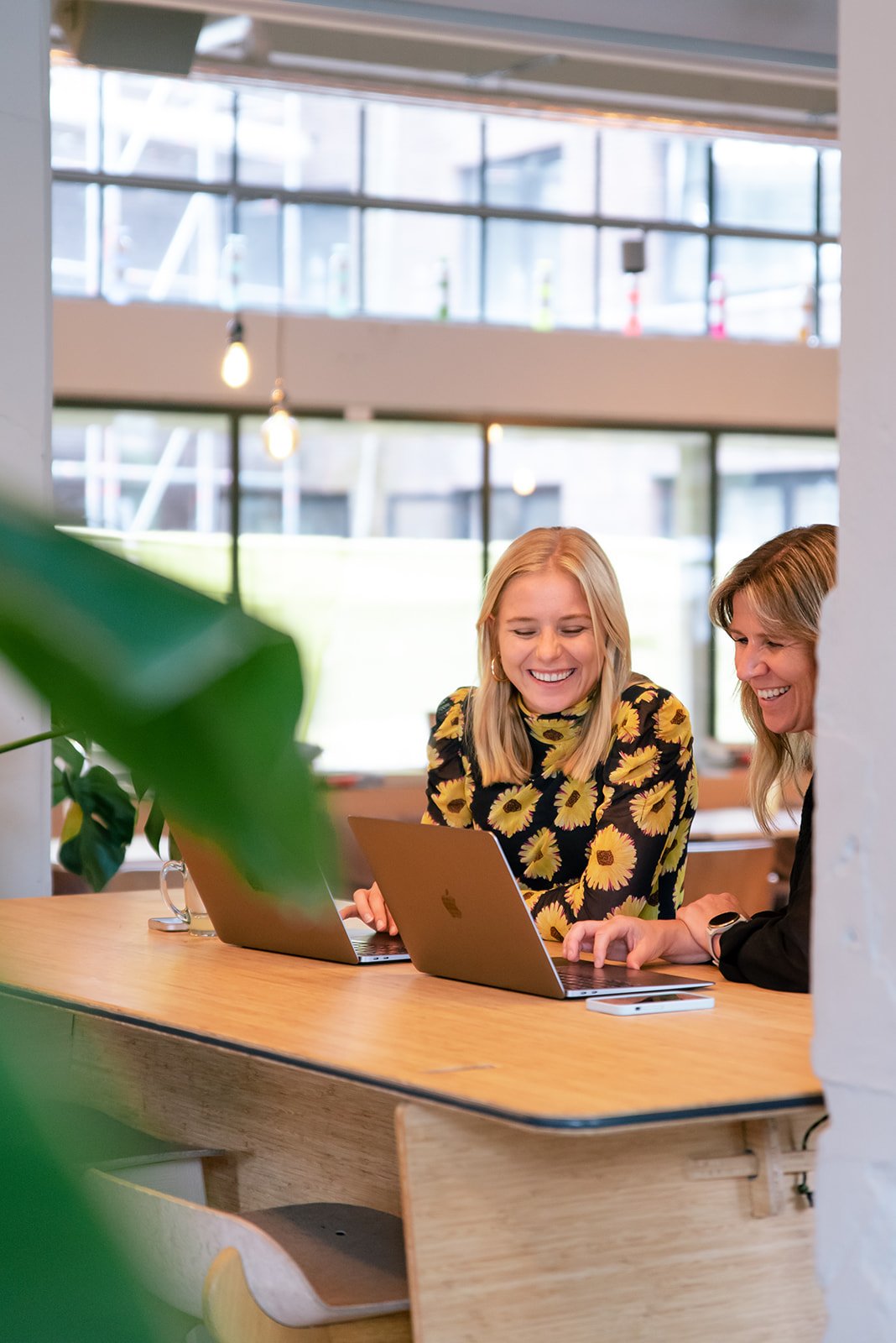 Twee vrouwelijke collega's werken lachend achter hun laptop