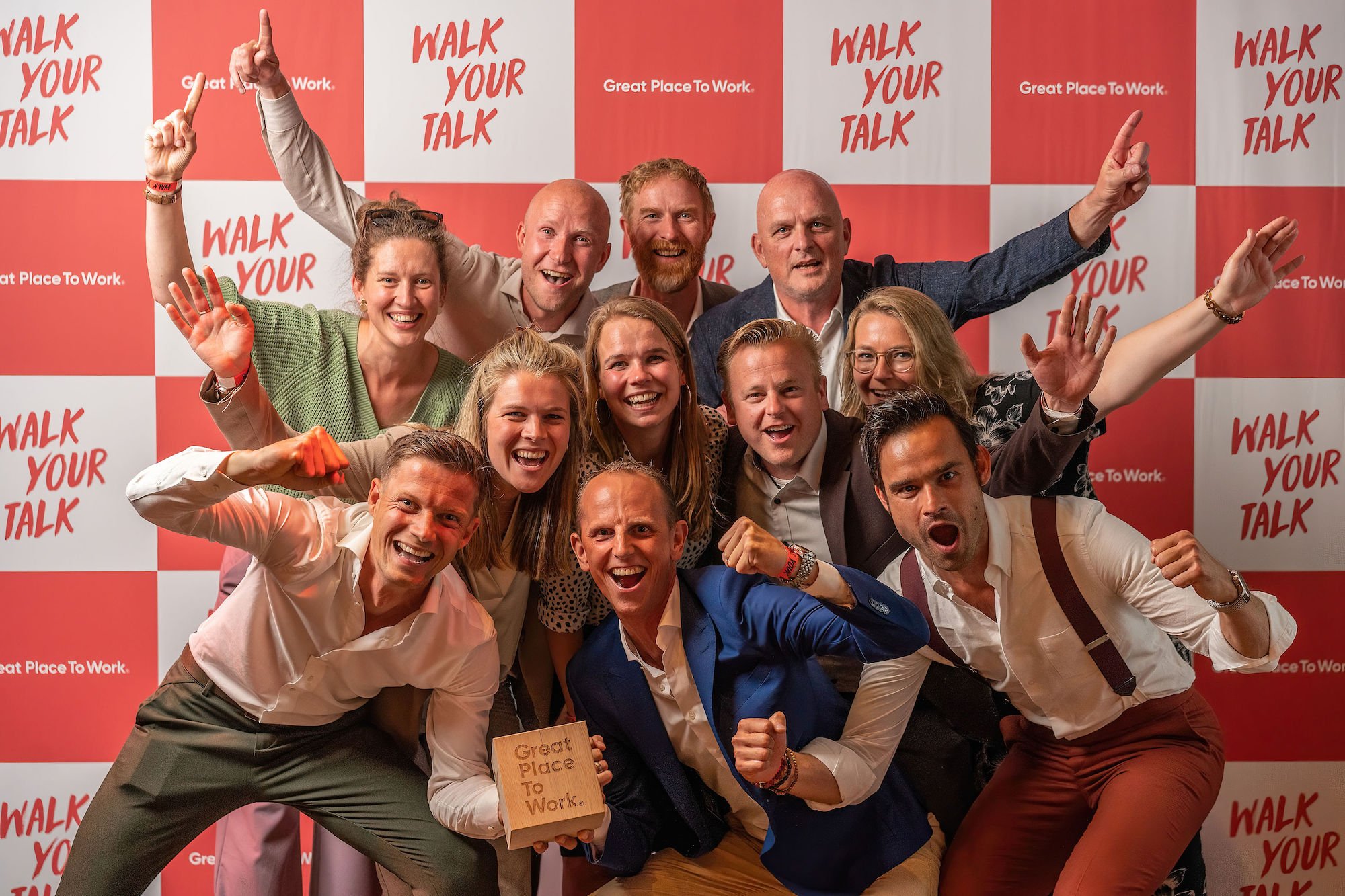 Blije medewerkers poseren voor fotowand tijdens uitreiking Best Workplaces