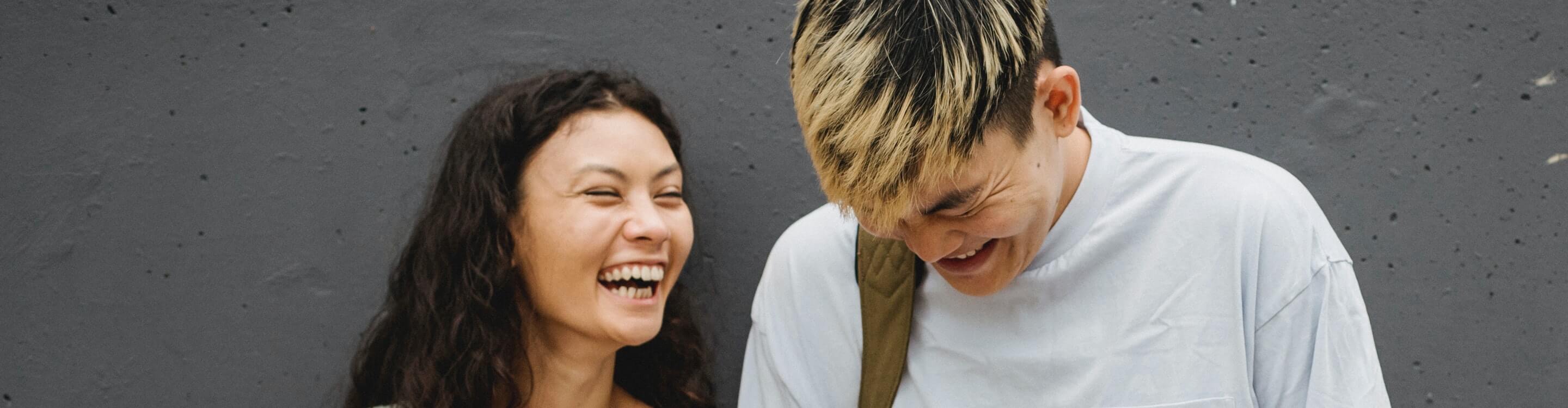 Twee mensen lachen hartelijk met elkaar tegenover een donkere achtergrond
